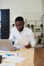 Young african executive in shirt sitting at his desk in the office, working online with laptop