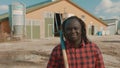 Young african farmer holding fork over the soulder and nodding his head in front of the silo system