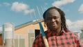 Young african farmerholding fork over the soulder and smiling in front of the silo system