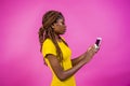 Young African female wiping a cellular phone on a light pink background