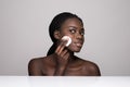 Young african girl applying foundation on her face using makeup sponge. Portrait of smiling african girl on white background