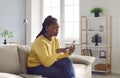 Young african girl with worried face expression using mobile phone while sitting on sofa at home. Royalty Free Stock Photo