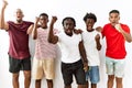 Young african group of friends standing together over isolated background angry and mad raising fist frustrated and furious while Royalty Free Stock Photo