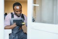 Young African Handyman In Uniform Fixing Glass Window With Screwdriver Royalty Free Stock Photo