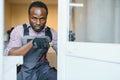 Young African Handyman In Uniform Fixing Glass Window With Screwdriver Royalty Free Stock Photo