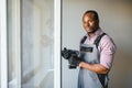 Young African Handyman In Uniform Fixing Glass Window With Screwdriver Royalty Free Stock Photo