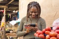 young african lady selling in a local african market using her mobile phone and credit card to do a transaction online Royalty Free Stock Photo