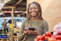 young african lady selling in a local african market using her mobile phone and credit card to do a transaction online smiling Royalty Free Stock Photo