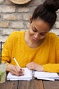 Young african lady sitting at cafe table and writing notes Royalty Free Stock Photo