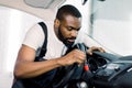 Young African male car wash detailing worker using cleaning brush and removing dust from car control panel. Car Royalty Free Stock Photo