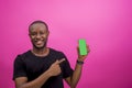 Young African male holding and pointing a cellular phone isolated on a light pink background