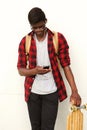 Young african male student standing against white wall with mobile phone and skateboard Royalty Free Stock Photo