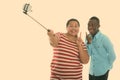 Happy young fat Asian woman and young black African man smiling while giving peace sign and taking selfie picture with Royalty Free Stock Photo