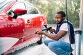 Young African man in casual wear washing his luxury car at self car wash station outdoors, using high pressure water Royalty Free Stock Photo