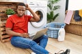 Young african man doing laundry and using computer confuse and wonder about question Royalty Free Stock Photo