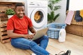 Young african man doing laundry and using computer with a happy and cool smile on face Royalty Free Stock Photo