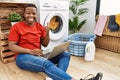 Young african man doing laundry and using computer doing happy thumbs up gesture with hand Royalty Free Stock Photo