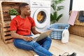 Young african man doing laundry and using computer looking to side, relax profile pose with natural face with confident smile Royalty Free Stock Photo