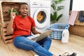 Young african man doing laundry and using computer pointing finger up with successful idea Royalty Free Stock Photo