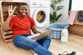 Young african man doing laundry and using computer showing and pointing up with fingers number four while smiling confident and