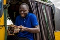 young african man driving a rickshaw taxi counting his money smiling