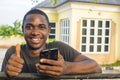 young african man holding his mobile phone smiling and giving a thumbs up Royalty Free Stock Photo