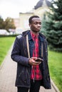 Young african man listening music in big headphones. Student relaxing, dreaming holding smart phone and earphones by hand. Travele