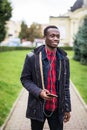 Young african man listening music in big headphones. Student relaxing, dreaming holding smart phone and earphones by hand. Travele Royalty Free Stock Photo