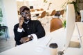 Young african man sitting at his desk talking on his mobile phone in office. African executive using cell phone while at work Royalty Free Stock Photo