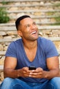 Young african man sitting outside using smart phone and looking up Royalty Free Stock Photo