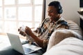 Young african man studying on laptop and writing down notes while sitting on couch Royalty Free Stock Photo