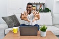 Young african man using laptop at home afraid and terrified with fear expression stop gesture with hands, shouting in shock Royalty Free Stock Photo