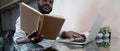 Young african man using laptop at home, black male looking at read book relaxing on leisure with work sit on glass table Royalty Free Stock Photo