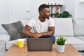 Young african man using laptop at home looking to side, relax profile pose with natural face with confident smile Royalty Free Stock Photo