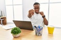 Young african man working at the office using computer laptop punching fist to fight, aggressive and angry attack, threat and Royalty Free Stock Photo