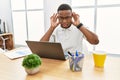 Young african man working at the office using computer laptop trying to hear both hands on ear gesture, curious for gossip Royalty Free Stock Photo