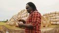 Young african man,working on tablet in front of the hay roll stack. Smart farming concept