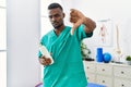 Young african physiotherapist man holding massage body lotion with angry face, negative sign showing dislike with thumbs down,