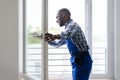 African Repairman In Overalls Installing Window