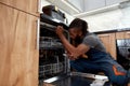 Young African repairman repairing dishwasher in kitchen, using screwdriver Royalty Free Stock Photo