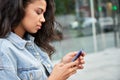 Young African teen girl standing on city street holding smart phone using apps. Royalty Free Stock Photo