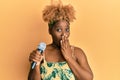 Young african woman with afro hair singing song using microphone covering mouth with hand, shocked and afraid for mistake Royalty Free Stock Photo