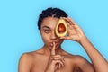 Beauty Concept. Young african woman isolated on blue covering eye with avocado showing silence gesture playful Royalty Free Stock Photo