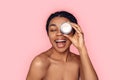 Beauty Concept. Young african woman isolated on pink covering eye with cream jar laughing cheerful Royalty Free Stock Photo