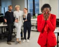 Young african woman crying because of the ridicule of colleagues. Racial discrimination in the office.