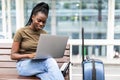 Young african woman with hand luggage in international airport terminal, working on her laptop while waiting for flight Royalty Free Stock Photo