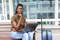 Young african woman with hand luggage in international airport terminal, working on her laptop while waiting for flight Royalty Free Stock Photo