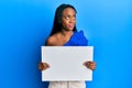 Young african woman holding blank empty banner smiling looking to the side and staring away thinking Royalty Free Stock Photo