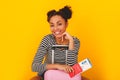 Young african woman isolated on yellow wall studio teen style traveler sitting on suitcase Royalty Free Stock Photo