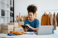 Young African woman running online store Startup small business SME, using smartphone or tablet taking receive and checking online Royalty Free Stock Photo